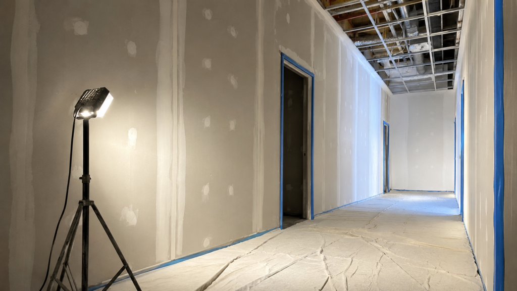 Condo corridor mid-repaint, drop sheets and wet paint sign on one side, walkway clear on the other