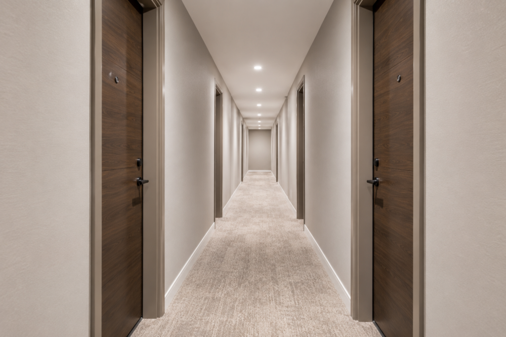 Freshly painted interior condominium corridor with warm greige walls, wood-look unit doors and even overhead recessed lighting