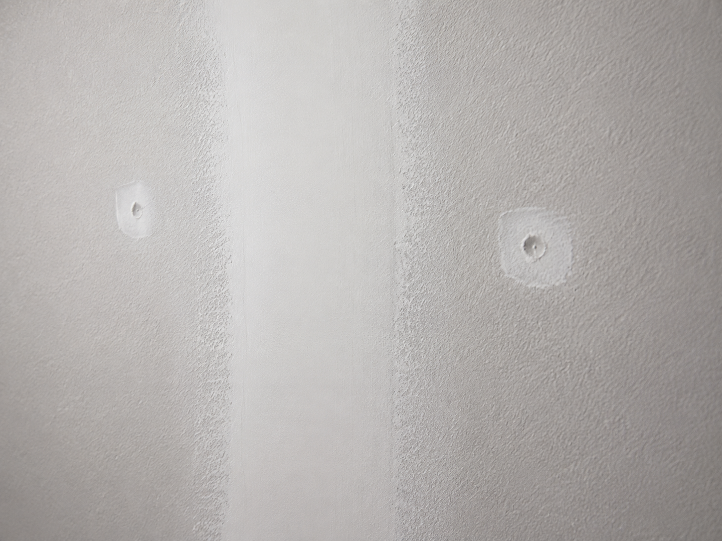 Extreme close-up of a taped and mudded drywall seam and two feathered screw indents finished smooth with white joint compound