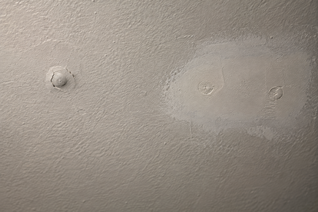 Drywall nail pop beside a refastened and patched repair